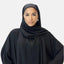 Eine Frau, gekleidet in einen schwarzen Hijab und eine Abaya von Elara, steht vor einem schlichten weißen Hintergrund und strahlt zeitlose Eleganz aus. Ihr Blick ist direkt und ihr Gesichtsausdruck neutral.