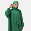 Eine Frau trägt einen leuchtend grünen Elara-Hijab und die passende Abaya. Sie posiert vor einem weißen Hintergrund, neigt den Kopf leicht und hält eine Hand ans Ohr. Sie strahlt zeitlose Eleganz aus und blickt selbstbewusst nach vorne.