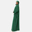 Eine Person, die in eine lange grüne Elara-Abaya und ein passendes Kopftuch gekleidet ist, steht seitlich vor einem schlichten Hintergrund. Der Stoff fällt sanft und strahlt durch sein elegantes und schlichtes Design zeitlose Eleganz aus.