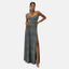 Eine Person in einem eleganten Abendkleid mit Metallic-Finish und hohem Schlitz steht selbstbewusst da. Mit einem eleganteren Ausschnitt trägt sie Hängeohrringe und High Heels und posiert mit einer Hand auf der Hüfte vor einem schlichten weißen Hintergrund.