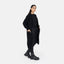 Vor weißem Hintergrund zeigt sich eine Frau im lässigen Look mit Oversize Cardigan, schwarzem Top, Pants und Lace-up-Boots von Elara. Mit den Händen in den Taschen strahlt sie Komfort und Selbstbewusstsein aus.
