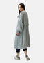 Eine Frau mit langen glatten Haaren präsentiert einen lässigen Look in einem hellgrauen Oversize-Cardigan von Elara, einer schwarzen Hose und weißen Sneakers. Sie steht über die Schulter gedreht vor einem schlichten weißen Hintergrund.