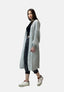 Eine Frau präsentiert einen lässigen Look mit einem hellgrauen Oversize Cardigan von Elara über schwarzem Crop Top und dunklen, gekrempelten Jeans – für maximalen Komfort, abgerundet mit weißen Sneakers vor hellem Hintergrund.