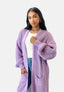Eine Frau im lässigen Look trägt einen Elara Oversize Cardigan in grobem Lavendel über einem weißen Top und Bluejeans und steht selbstbewusst vor einem schlichten hellgrauen Hintergrund.
