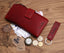 Eine chunkyrayan rote Leder-Geldbörse im Vintage-Look ist zusammen mit Banknoten, Münzen, Schlüsselanhänger, Brille, Taschenuhr und Karten auf einer Holzoberfläche arrangiert.