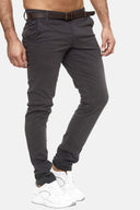 Ein Mann in dunkelgrauer Slim-Fit-Hose, braunem Gürtel und weißen Turnschuhen steht vor einem schlichten hellen Hintergrund. Sein Oberkörper ist nicht sichtbar.