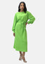 Ein Elara-Kleid in leuchtendem Grün mit langen Ärmeln und gebundener Taille verkörpert Eleganz, während die Frau anmutig posiert. Sie vervollständigt ihren Look mit silbernen Riemchen-Pumps und Ohrhängern vor einem schlichten weißen Hintergrund.