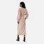 Eine elegante Frau mit langem, dunklem Haar blickt abgewandt in einem hellrosa Elara-Kleid, das in der Taille gebunden wird und an eine Abaya erinnert. Ihr Look wird durch schwarze Stöckelschuhe vor einem schlichten weißen Hintergrund abgerundet.