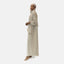 Against a plain background, an individual wears the Elara Damen Abaya mit Kopftuch in light beige with subtle golden details, paired with a matching hijab. Their calm expression and white high-heeled sandals enhance the Komfort of their elegant ensemble.