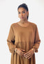 Mit zurückgebundenem dunklen Haar trägt sie ein Elara Damen Abaya Maxikleid aus Polyesterstoff mit goldenen Ringen und Ohrringen und verströmt damit orientalischer Flair. Sie steht vor einem schlichten weißen Hintergrund.