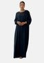 Eine Person in einem Elara Damen Abaya Maxikleid aus eleganter Polyesterfaser steht vor einem schlichten Hintergrund. Das lange schwarze Kleid strahlt orientalische Raffinesse aus, gepaart mit goldenen Ohrringen und Armbändern, die Hände sanft vor der Brust verschränkt.