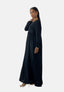 Eine Frau steht in einem langen schwarzen Elara Damen Abaya Maxikleid vor einem schlichten Hintergrund und strahlt orientalische Raffinesse aus. Sie trägt Creolen, ein Armband und Riemchen-High-Heels, ihr Haar ist elegant zurückgekämmt.
