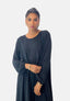 Mit Creolen und Armbändern von Elara strahlt diese Person in einem langärmeligen, schwarzen Damen-Abaya-Maxikleid orientalische Raffinesse aus. Sie steht mit ruhigem Blick vor einem schlichten weißen Hintergrund.