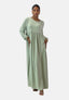 Eine Person steht selbstbewusst da und trägt ein langes, hellgrünes Damen Abaya Maxikleid von Elara. Es hat lange Ärmel und Taschen. Creolen, offene Sandalen und zurückgebundene Haare runden das Kleid ab. Der Polyesterstoff verleiht dem schlichten weißen Hintergrund ein orientalisches Flair.