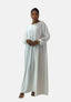 Eine Frau trägt ein langes, fließendes Elara Damen Abaya Maxikleid in Weiß mit Puffärmeln. Goldene Ohrringe und Armbänder schmücken sie, während ihr Haar elegant nach hinten gekämmt ist und vor einem schlichten weißen Hintergrund orientalische Raffinesse verkörpert.