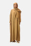 Eine Frau präsentiert elegant eine lange, fließende, kamelfarbene Abaya und ein passendes Kopftuch von Elara vor einem schlichten Hintergrund. Goldene High Heels ergänzen das Ensemble und strahlen mit den entspannten Händen zeitlose Eleganz aus.