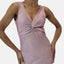 Person, die ein ärmelloses, glitzerndes rosa Abendkleid mit tiefem V-Ausschnitt und gedrehtem Vorderdetail trägt und vor einem schlichten weißen Hintergrund posiert.