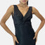 Eine Person präsentiert ein Abendkleid – ein ärmelloses, schimmerndes schwarzes Kleid mit verdrehtem Frontdesign. Der tiefe V-Ausschnitt unterstreicht die selbstbewusste Pose, die Hände in die Hüften gestemmt vor einem schlichten weißen Hintergrund.