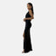 Eine Person posiert elegant in einem eleganten, bodenlangen, schwarzen Abendkleid mit hohem Schlitz und ärmellosem Schnitt. Die silbernen Pumps ergänzen den Look, während die langen, dunklen Haare zurückgekämmt sind. Der Hintergrund ist schlicht weiß und unterstreicht den luxuriösen Reiz des Kleides.