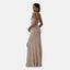 Eine Frau in einem schimmernden, ärmellosen, bodenlangen Abendkleid mit offenem Rücken posiert elegant. Sie steht im Profil, eine Hand auf der Hüfte, und präsentiert den seitlichen Schlitz des Kleides. Ihr dunkles Haar ist nach hinten frisiert, und sie trägt große Creolen. Das Kleid aus weichem Polyester fällt anmutig.