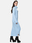 Eine Frau steht seitlich in einem langen, hellblauen Rippstrickkleid mit Rollkragen und langen Ärmeln. Ihren Herbst- und Wintergarderobe-Look ergänzt sie mit schwarzen Plateaustiefeletten vor schlichtem weißem Hintergrund.