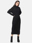 Die Person trägt ein langes schwarzes Strickkleid mit Rollkragen und langen Ärmeln. Sie hat lange Haare und steht selbstbewusst mit den Händen in den Hüften. Schwarze Stiefeletten runden das Outfit ab, perfekt passend zur Herbst- und Wintergarderobe vor dem schlichten weißen Hintergrund.