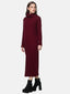 Eine Frau in einem langen, dunkelroten Rollkragen-Strickkleid steht vor einem schlichten, hellen Hintergrund und verkörpert die Essenz der Herbst- und Wintergarderobe. Sie ergänzt ihren Look mit schwarzen Plateaustiefeletten und hat langes, glattes braunes Haar. Ihr Blick schweift mit neutralem Ausdruck leicht zur Seite.