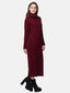 Eine Frau in einem langen, burgunderfarbenen Strickkleid mit Rollkragen und schwarzen Plateau-Heels posiert vor einem schlichten weißen Hintergrund und blickt mit einem leichten Lächeln in die Kamera – eine perfekte Ergänzung für Ihre Herbst- und Wintergarderobe.