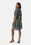 Eine Frau in einem schwarzen Damenkleid mit Blumenmuster von Elara und schwarzen Riemchensandaletten steht leicht gedreht da und blickt über ihre Schulter vor einem schlichten hellen Hintergrund – ein idealer Look für den Sommer.