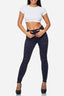 Eine Frau steht in einer schlichten weißen Umgebung und blickt nach vorne. Sie trägt ein kurzes weißes T-Shirt von Elara, dunkle Skinny Jeans im Used-Look und schwarze High Heels und hat ihre Hände am Bund ihrer Jeans.