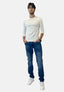 Ein Mann steht mit den Händen in den Taschen vor einem schlichten weißen Hintergrund und trägt eine Elara-Brille, ein weißes Langarmhemd, Bluejeans und weiße Turnschuhe.