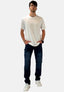 Ein Mann steht mit dem Gesicht nach vorne, hat die Hände in den Jeanstaschen und trägt ein schlichtes weißes T-Shirt von Elara, dunkelblaue Jeans, weiße Turnschuhe und eine Brille vor einem schlichten weißen Hintergrund.