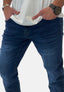 Eine Person in einem weißen Elara-Shirt und dunkelblauen Jeans steht mit den Händen in den Taschen da. Sie trägt eine schwarze Armbanduhr und ein silbernes Armband. Der Hintergrund ist schlicht weiß.