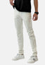 Ein Mann in cremefarbenen Slim-Fit-Jeans von Elara, einem schwarzen T-Shirt, weißen Turnschuhen mit schwarzen Streifen und einer schwarzen Armbanduhr steht vor einem schlichten weißen Hintergrund.