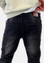 Person in hellem Sweatshirt und schwarzer Elara Waschlook Jeans, von der Taille abwärts und von hinten gesehen, ein brauner Lederpatch am Hosenbund unterstreicht die bequeme Passform.