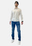 Ein junger Mann mit Brille, weißem Hemd mit Knöpfen, blauen Jeans von Elara in Waschlook und bequemer Passform sowie weißen Turnschuhen steht mit leicht nach oben gerichtetem Blick vor einem schlichten weißen Hintergrund.