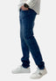Eine Person trägt blaue Jeans im Waschlook von Elara mit bequemer Passform, ein weißes Hemd, ein schwarzes Armbanduhr und weiße Sneakers mit schwarzen Streifen und steht mit einer Hand in der Tasche vor weißem Hintergrund.