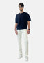 Ein Mann präsentiert ein schwarzes Elara-T-Shirt, trendige weiße Jeans im verwaschenen Look und weiße Sneakers vor einem schlichten Hintergrund. Er trägt kurze dunkle Haare, Brille, Uhr und Armbänder – ein Style mit moderner Passform.