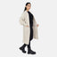 Eine Frau steht vor einem weißen Hintergrund und trägt einen Elara Oversize Cardigan für maximalen Komfort über einem schwarzen Outfit mit klobigen schwarzen Stiefeln, ihre Hände in den Cardigan-Taschen für einen lässigen Look.