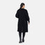 Eine Frau mit dunklem Haar trägt im lässigen Look einen langen schwarzen Oversize-Cardigan von Elara, schwarze Leggings und schwarze Stiefel und steht mit dem Rücken vor einem schlichten weißen Hintergrund.