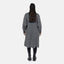 Eine Person steht mit abgewandtem Gesicht und trägt einen langen grauen Elara Oversize Cardigan für maximalen Komfort, kombiniert mit schwarzen Leggings und Stiefeletten vor einem schlichten weißen Hintergrund.