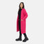 Eine Frau steht im entspannten Look vor weißem Hintergrund und trägt einen Elara Oversize Cardigan in leuchtendem Pink über einem schwarzen Outfit mit Schnürstiefeln. Ihre langen dunklen Haare und ihr leichtes Lächeln strahlen maximale Gemütlichkeit aus.