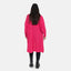 Eine Person mit langem, dunklem Haar steht mit abgewandtem Gesicht da und trägt für maximalen Komfort eine leuchtend rosa Oversize-Strickjacke von Elara, kombiniert mit schwarzen Leggings und Stiefeln vor einem schlichten weißen Hintergrund.