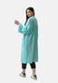 Eine Frau präsentiert einen lässigen Look in einem langen, hellblauen Oversize-Cardigan mit Fronttaschen von Elara, einer schwarzen Hose und weißen Sneakers. Sie steht mit dem Gesicht abgewandt und blickt über ihre Schulter vor einem schlichten weißen Hintergrund.