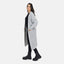 Eine Frau steht seitlich in einem Elara Oversize Cardigan in Hellgrau über einem schwarzen Outfit und klobigen Stiefeln, die Hände in den Taschen, und betont maximalen Komfort und einen lässigen Look vor weißem Hintergrund.