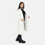 Eine Frau posiert in einem langen, weißen Oversize Cardigan mit Taschen von Elara, kombiniert mit schwarzem Shirt, schwarzer Hose und schwarzen Chunky Boots vor schlichtem weißen Hintergrund für einen lässigen Look.