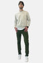Ein Mann steht mit Blick nach vorne da, trägt eine Brille, ein beiges Sweatshirt über einem weißen Hemd, eine Elara Slim Fit Chino-Hose für optimalen Komfort und weiße Turnschuhe, die Hände in den Taschen vor einem schlichten weißen Hintergrund – ein müheloser Allround-Look.