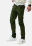 Eine Person in olivgrüner Elara Slim Fit Chino-Hose, weißem Langarmhemd, schwarzer Armbanduhr und weißen Turnschuhen steht vor einem schlichten weißen Hintergrund und unterstreicht modernen Tragekomfort.