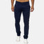 Ein Mann trägt eine Elara Slim Fit Chino-Hose in Marineblau und weiße Sneakers. Seine Hände stecken in den Hosentaschen vor einem schlichten hellgrauen Hintergrund, sein Oberkörper ist nicht sichtbar.