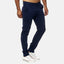 Ein Mann trägt eine Elara Slim Fit Chino-Hose in Marineblau mit weißen Low-Top-Sneakers, die Hände in den Taschen und stellt so mühelos seinen Komfort vor einem schlichten hellgrauen Hintergrund zur Schau.